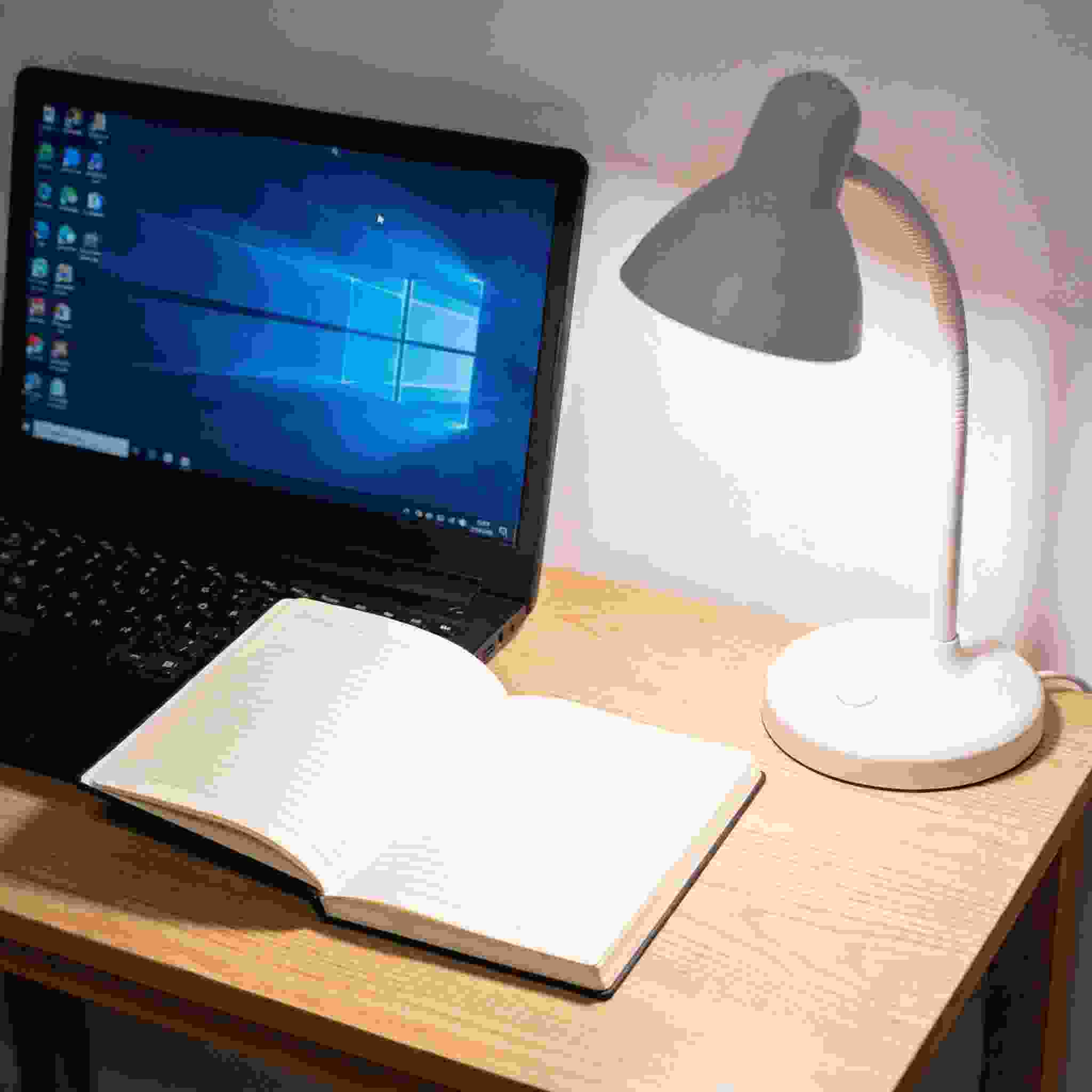 电脑桌上的笔记本，屏幕显示Windows界面，旁边放着台灯