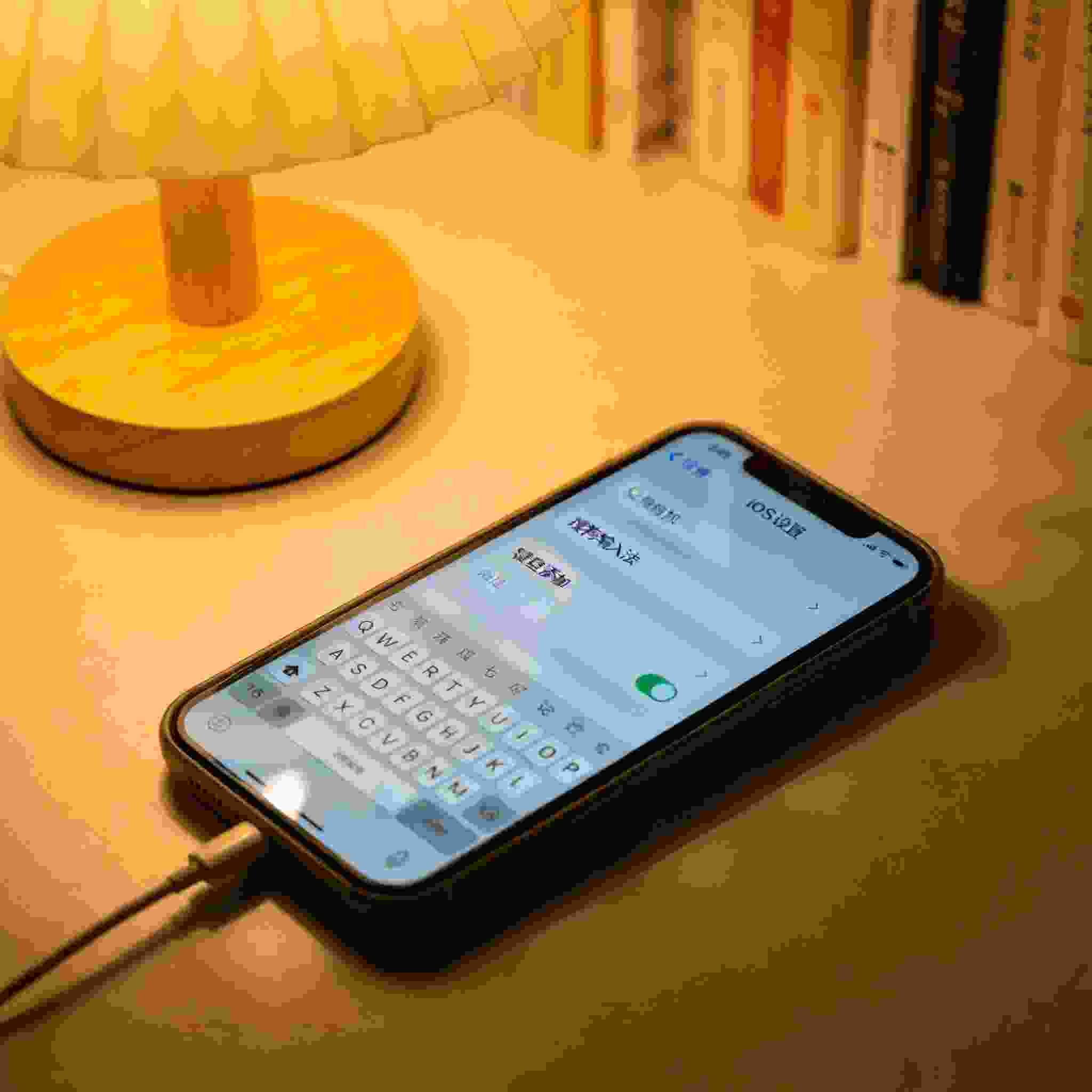 书桌的iPhone，屏幕显示iOS系统设置的键盘添加界面，已选中搜狗拼音输入法，桌面角落有个充电线，台灯暖光