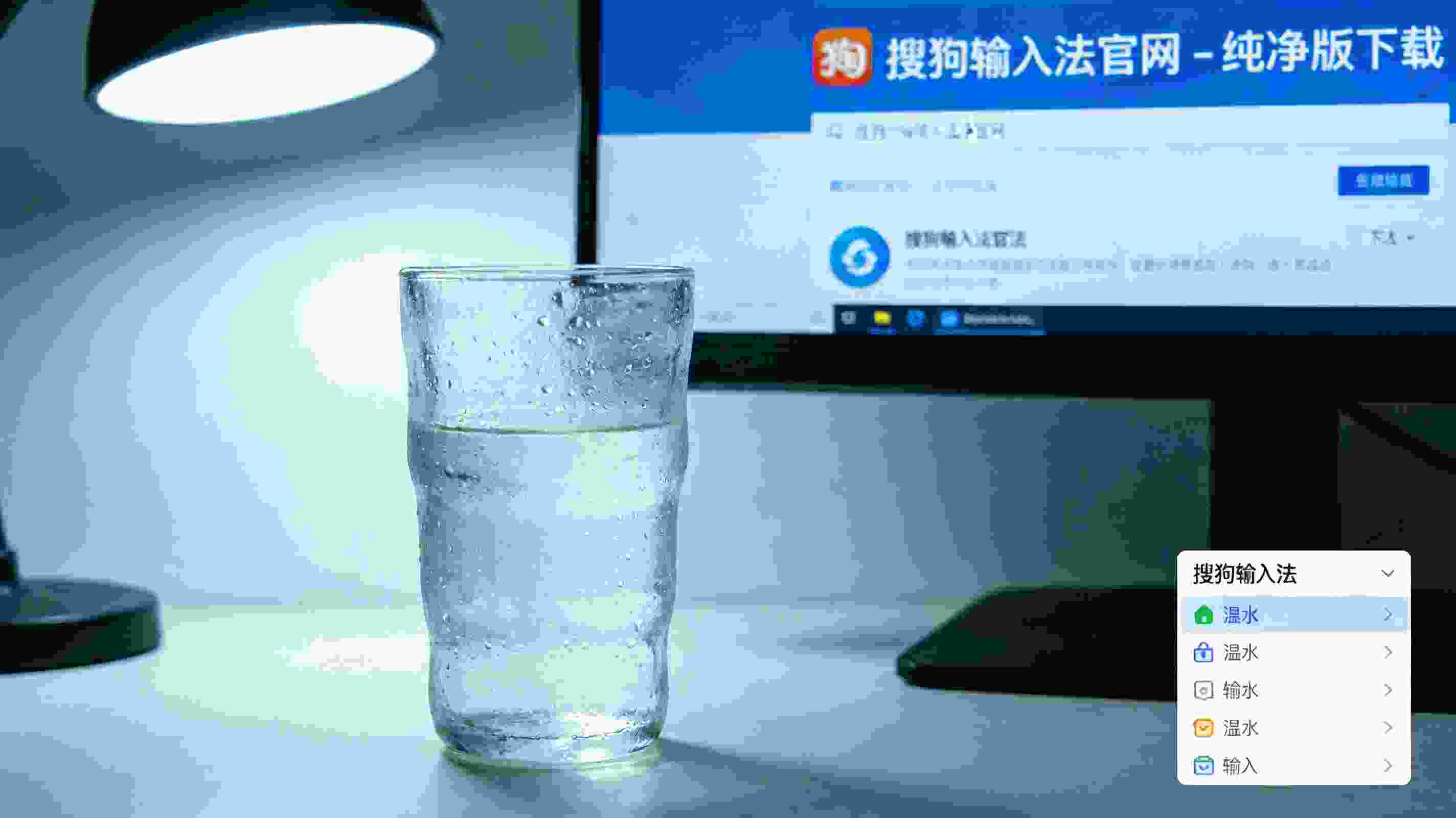 电脑屏幕显示搜狗拼音输入法官网的纯净版下载页面，桌面右下角的输入法列表里显示搜狗拼音输入法，旁边放着半杯温水，台灯冷光