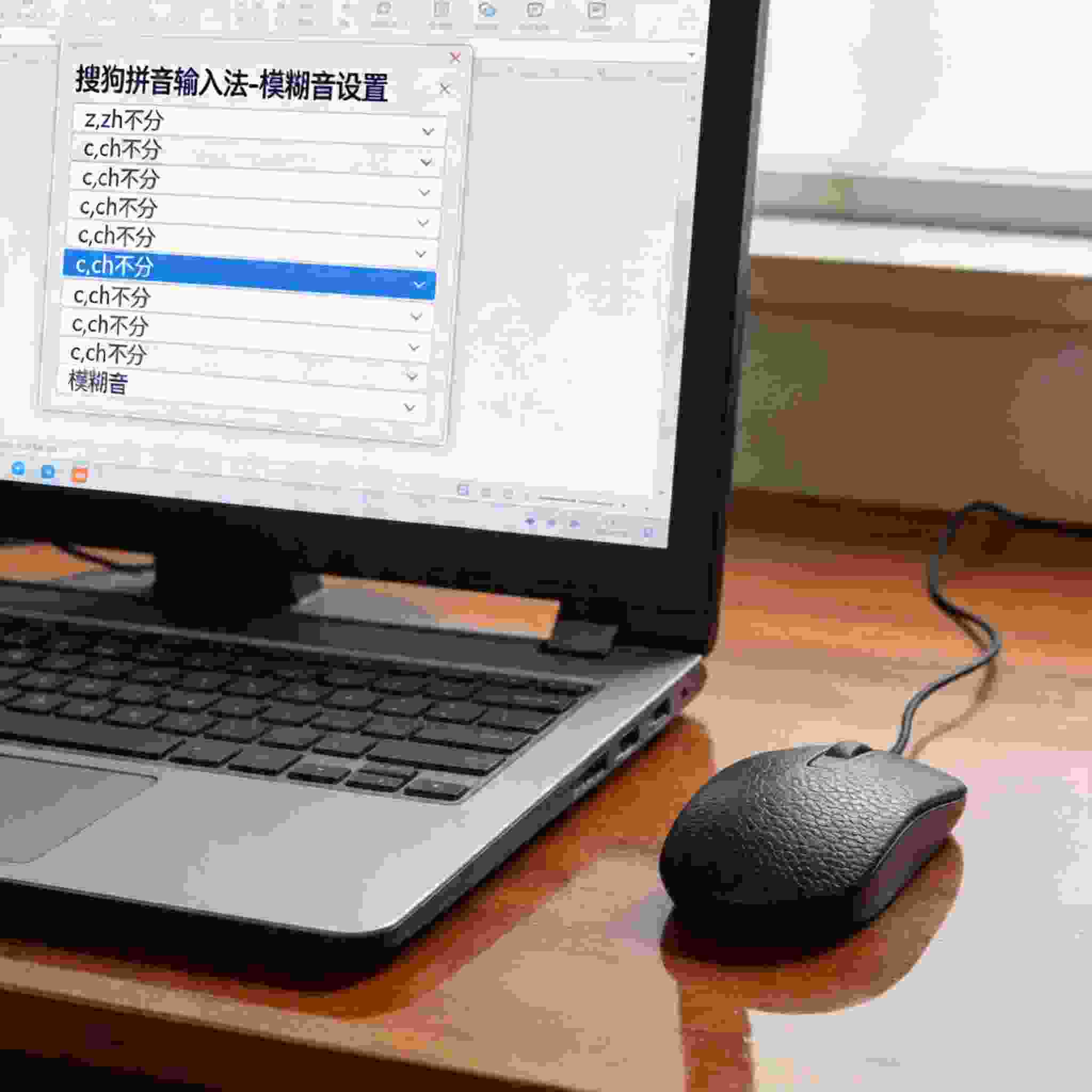 电脑放在桌面上，屏幕显示搜狗拼音输入法的模糊音设置界面，旁边放着鼠标，室内自然光