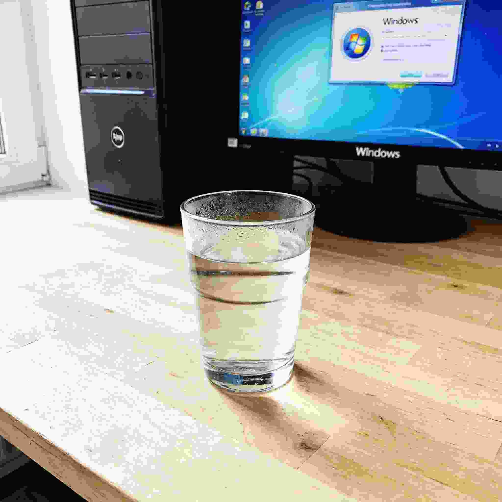 书桌上的主机，屏幕显示Windows设置界面，桌角放着水杯，自然光