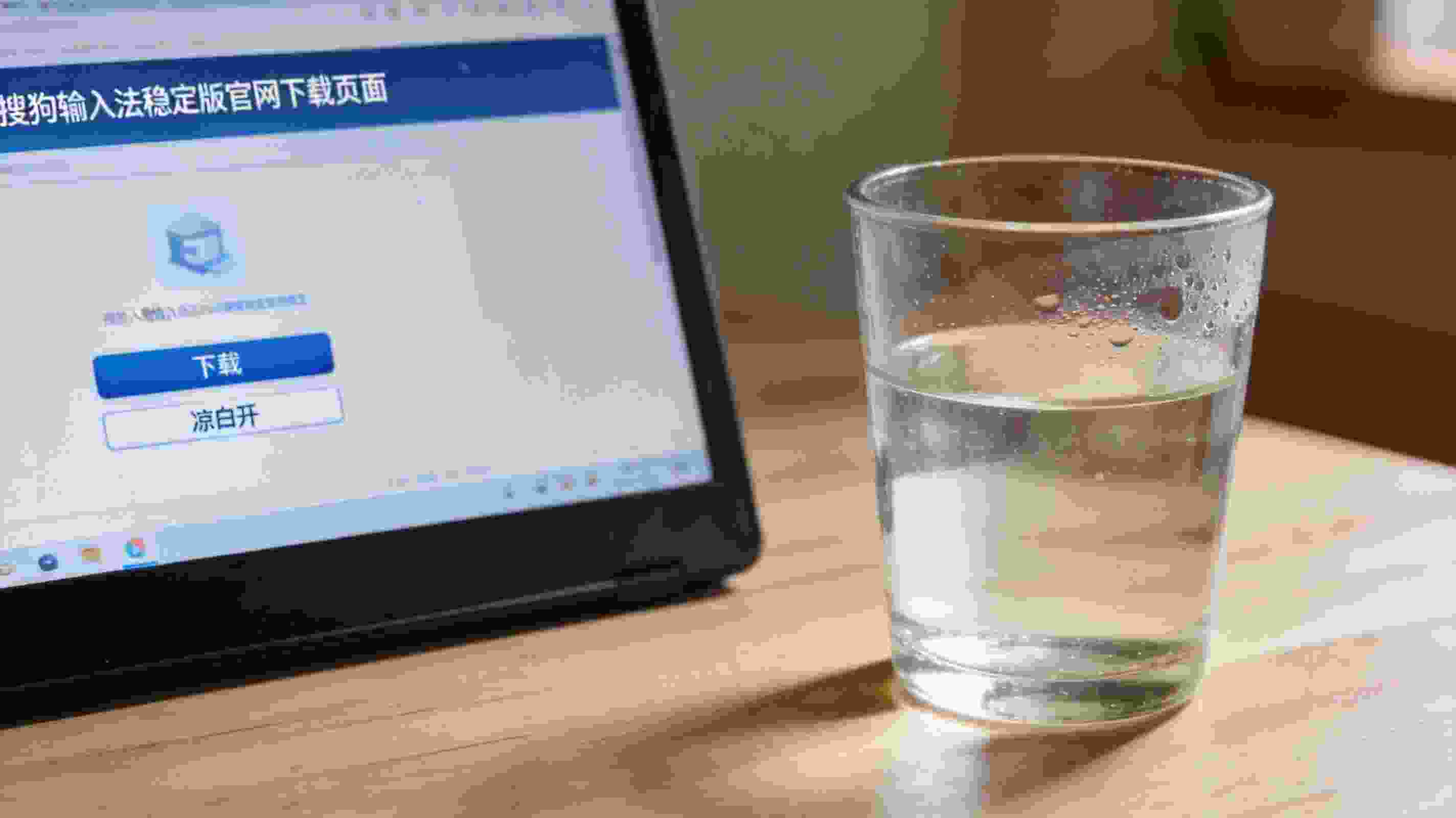 电脑桌面显示搜狗拼音输入法稳定版官网下载页面，旁边放着半杯凉白开，室内自然光