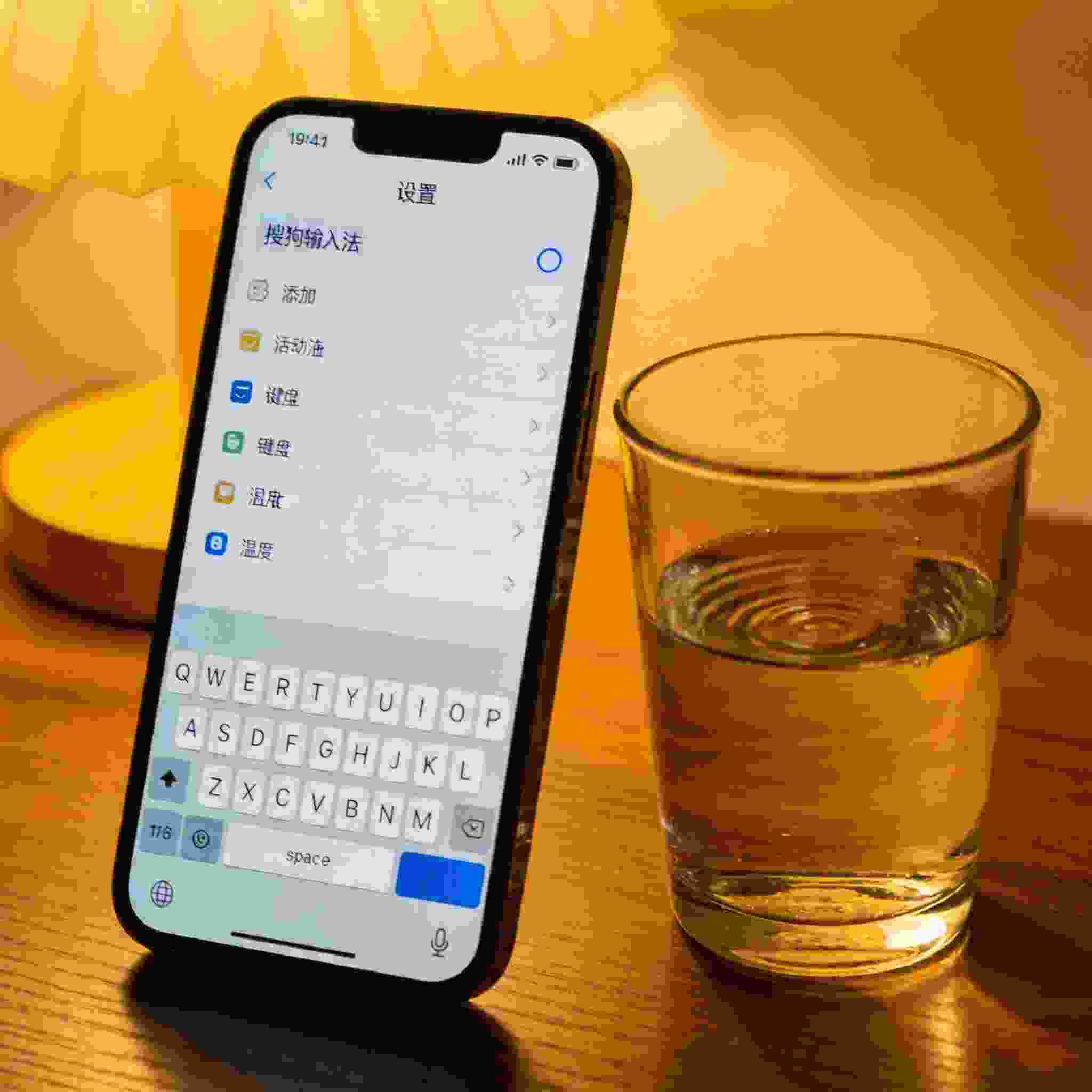桌面的iPhone屏幕显示设置里的键盘添加界面，已选中搜狗拼音输入法，旁边放着半杯温水，台灯暖光
