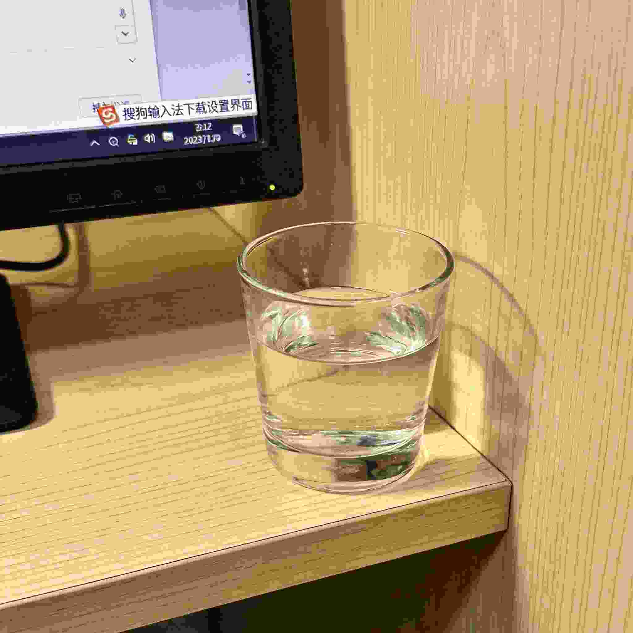 书桌上的电脑，屏幕显示搜狗拼音输入法下载设置界面，桌角放着水杯，自然光