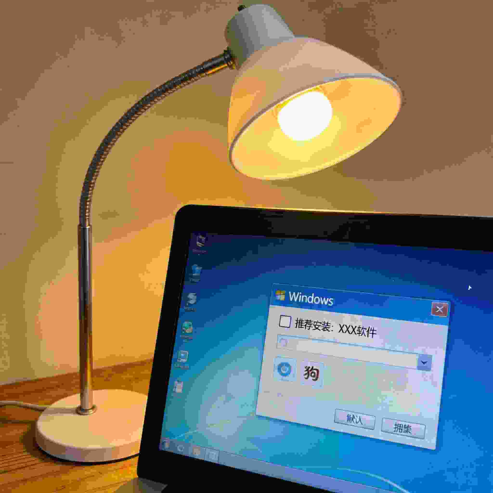 电脑屏幕显示Windows系统下搜狗拼音输入法的安装界面，界面上有默认勾选的捆绑软件选项，旁边桌面有一个台灯，台灯开着暖光