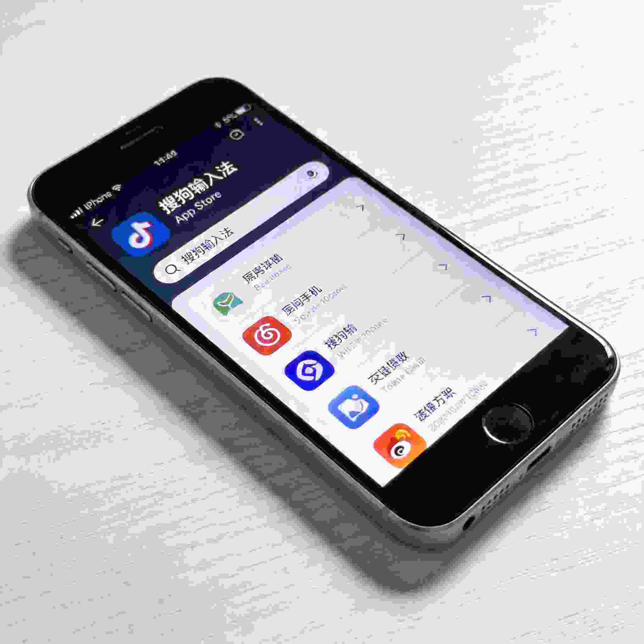 桌面放着iPhone，屏幕显示App Store界面，搜索栏输入“搜狗拼音输入法”，下方显示对应应用下载选项，室内自然光