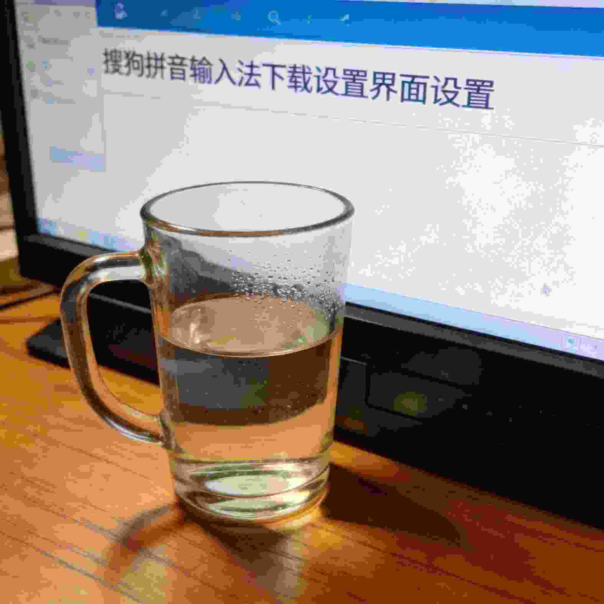 书桌上的主机，屏幕显示搜狗拼音输入法下载设置界面，桌角放着水杯，自然光