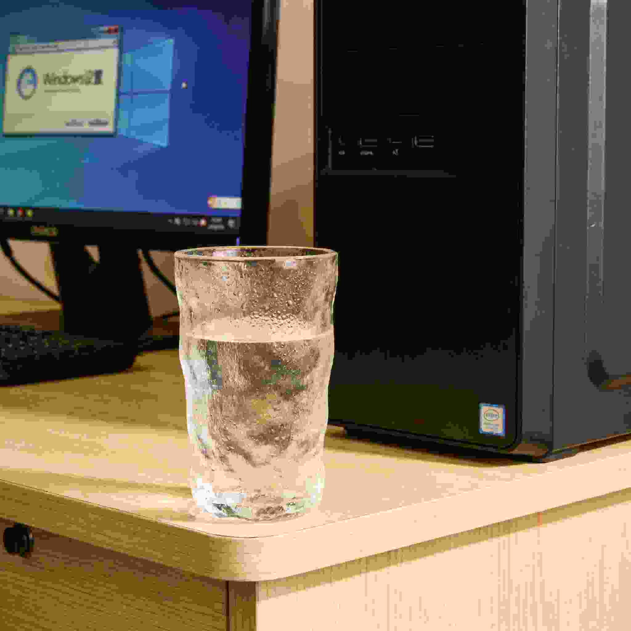 书桌上的主机，屏幕显示Windows设置界面，桌角放着水杯，自然光