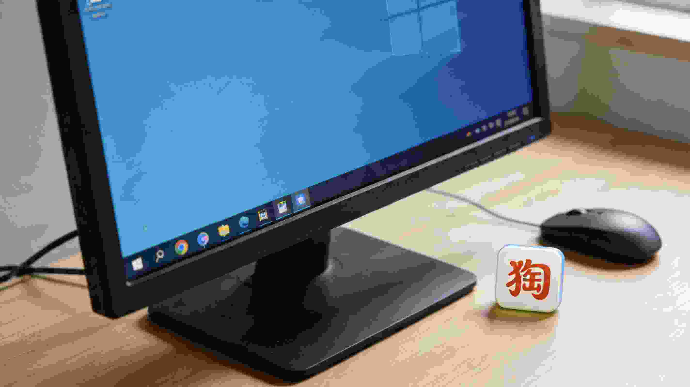 电脑桌面，屏幕显示Windows系统任务栏的搜狗拼音输入法图标，旁边放着鼠标，室内自然光