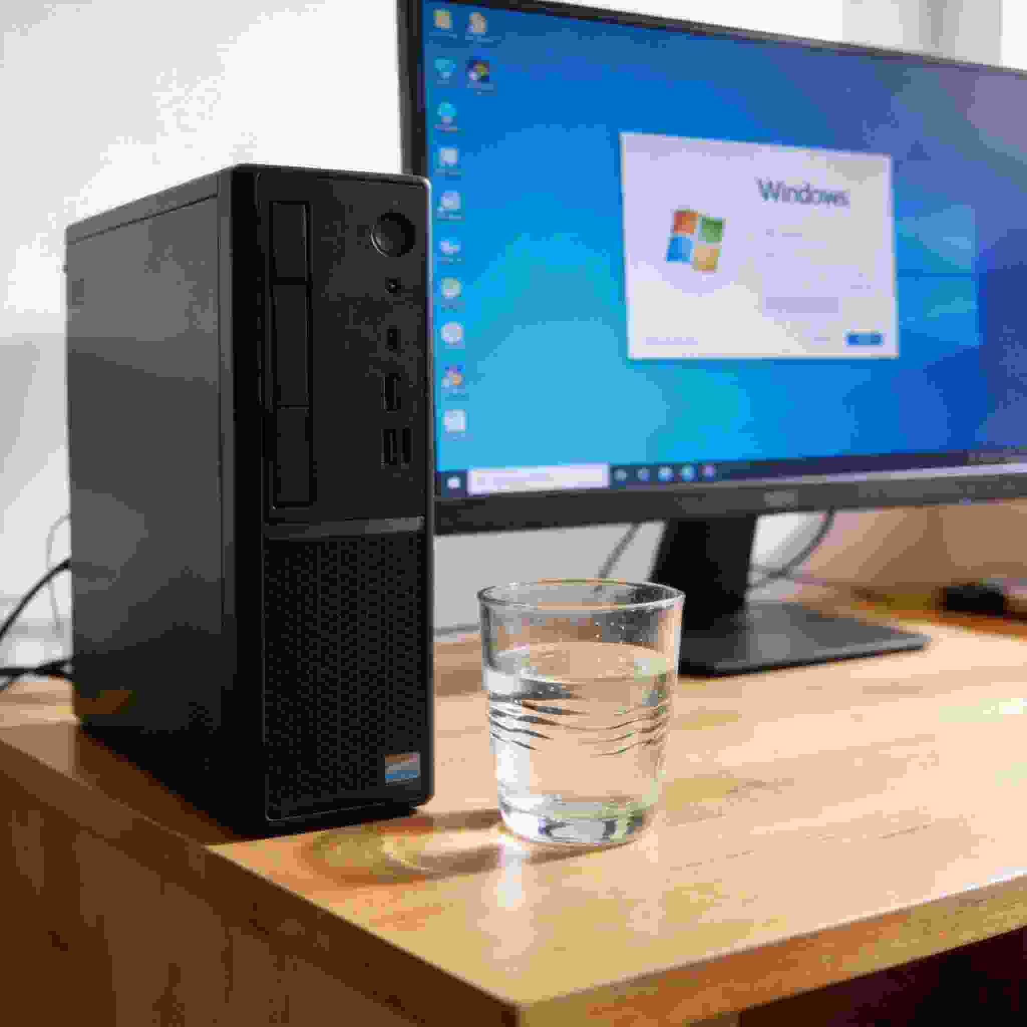 书桌上的主机，屏幕显示Windows设置界面，桌角放着水杯，自然光