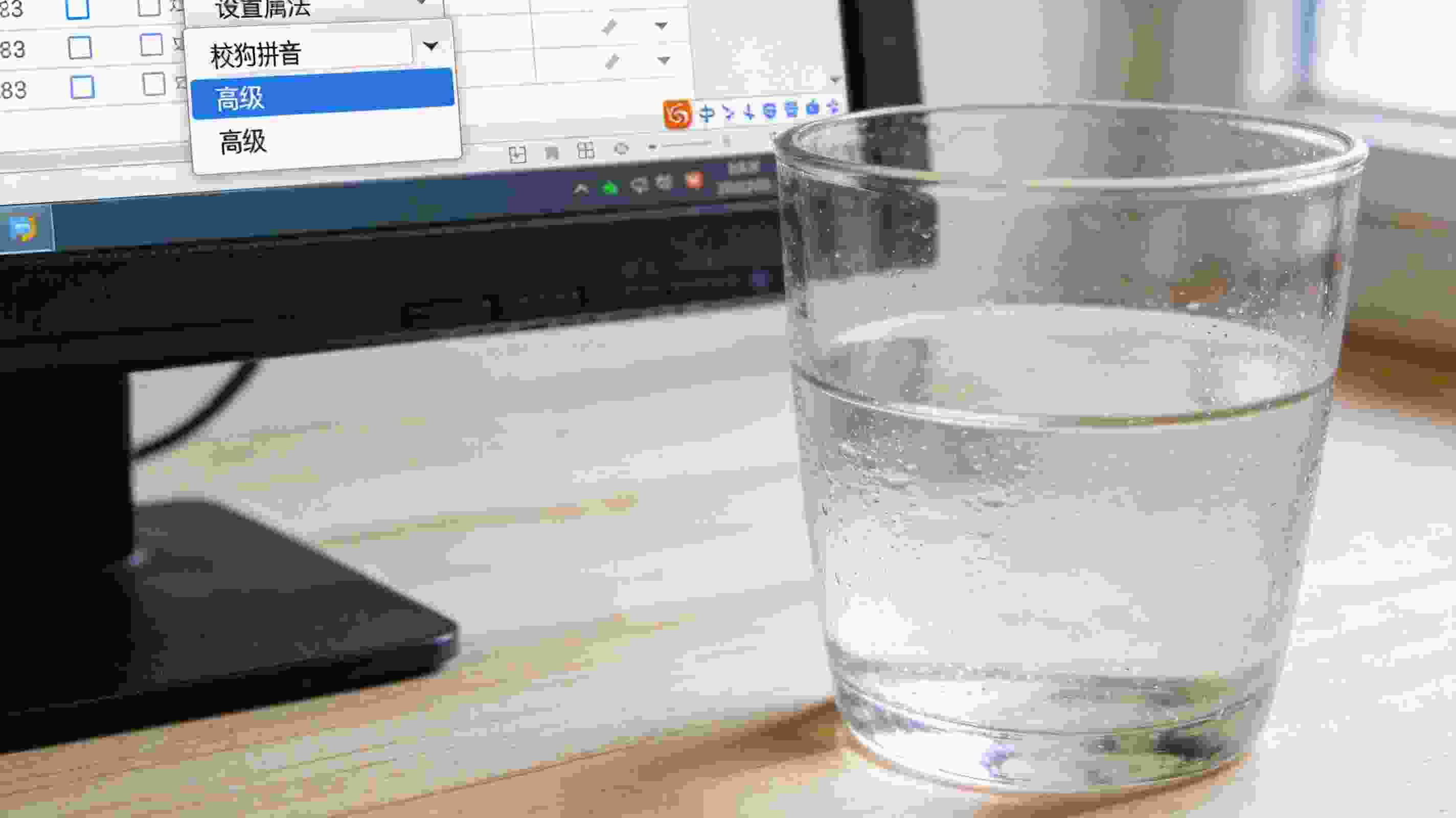 电脑桌面，屏幕显示搜狗拼音输入法的设置属性界面，选中“高级”选项卡，旁边放着半杯凉白开，室内自然光