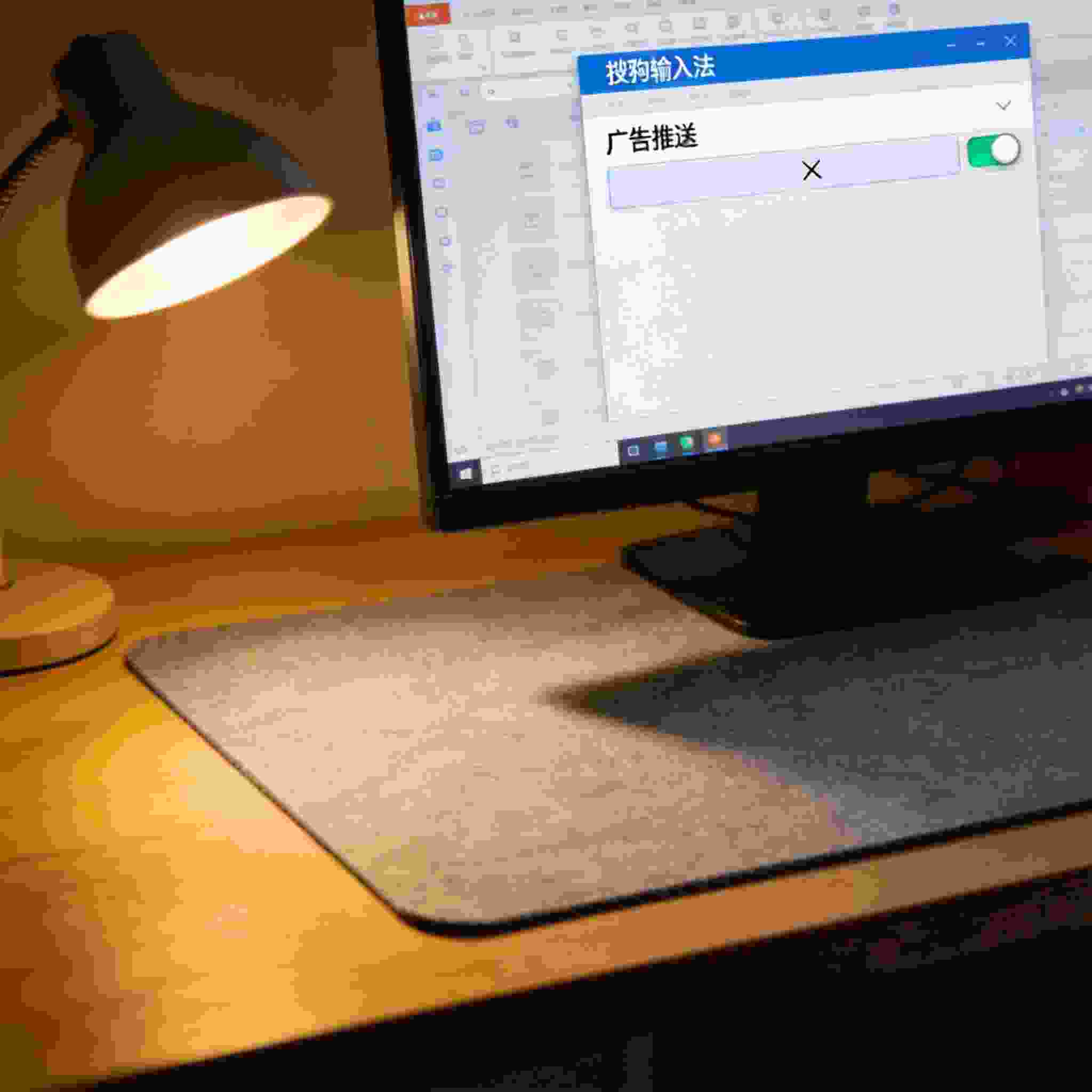电脑屏幕显示搜狗拼音输入法设置界面，界面里的广告推送选项已关闭，桌面铺着浅灰色桌垫，台灯暖光