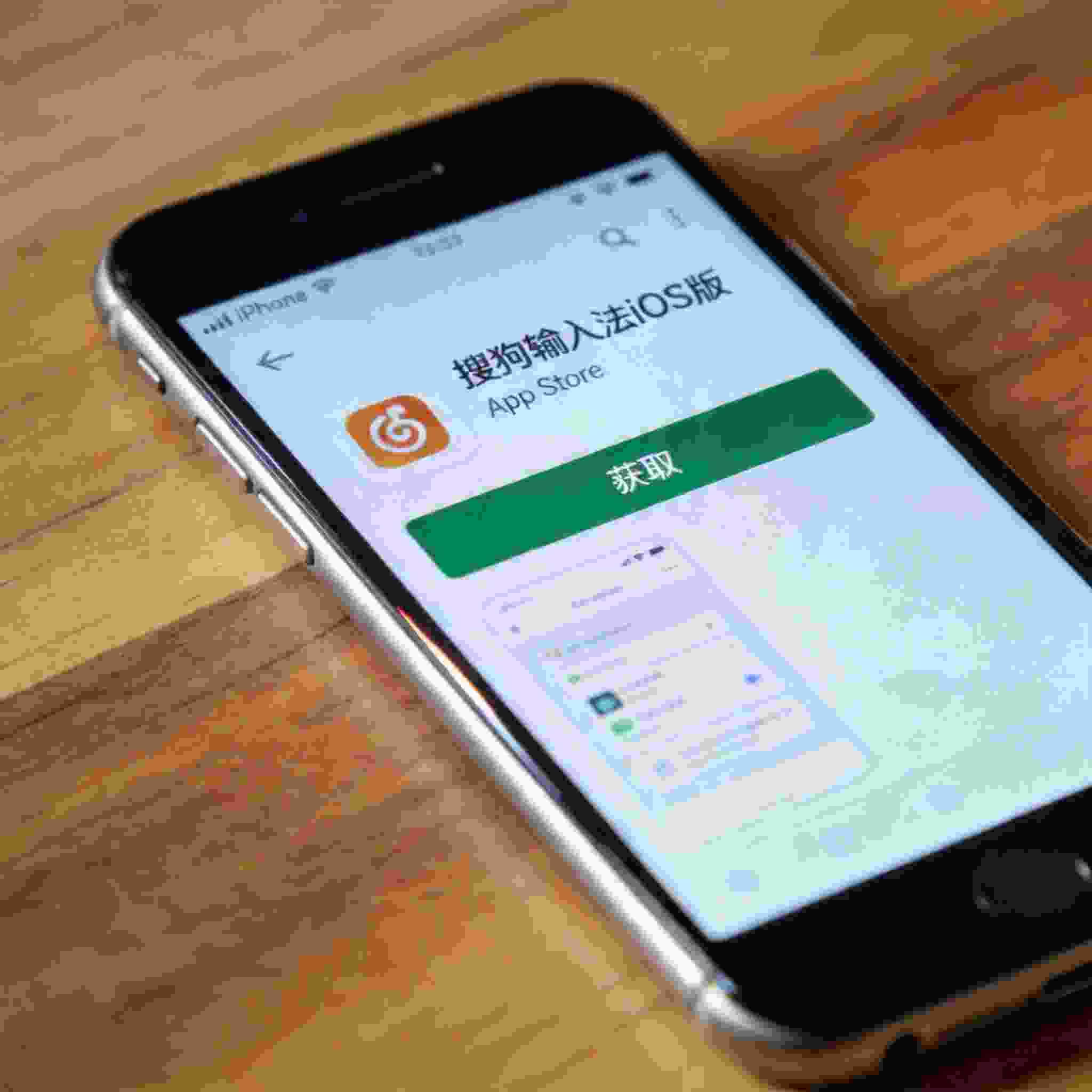 桌面放着iPhone，屏幕显示App Store里的搜狗拼音输入法iOS版下载界面，下方有获取按钮，室内自然光
