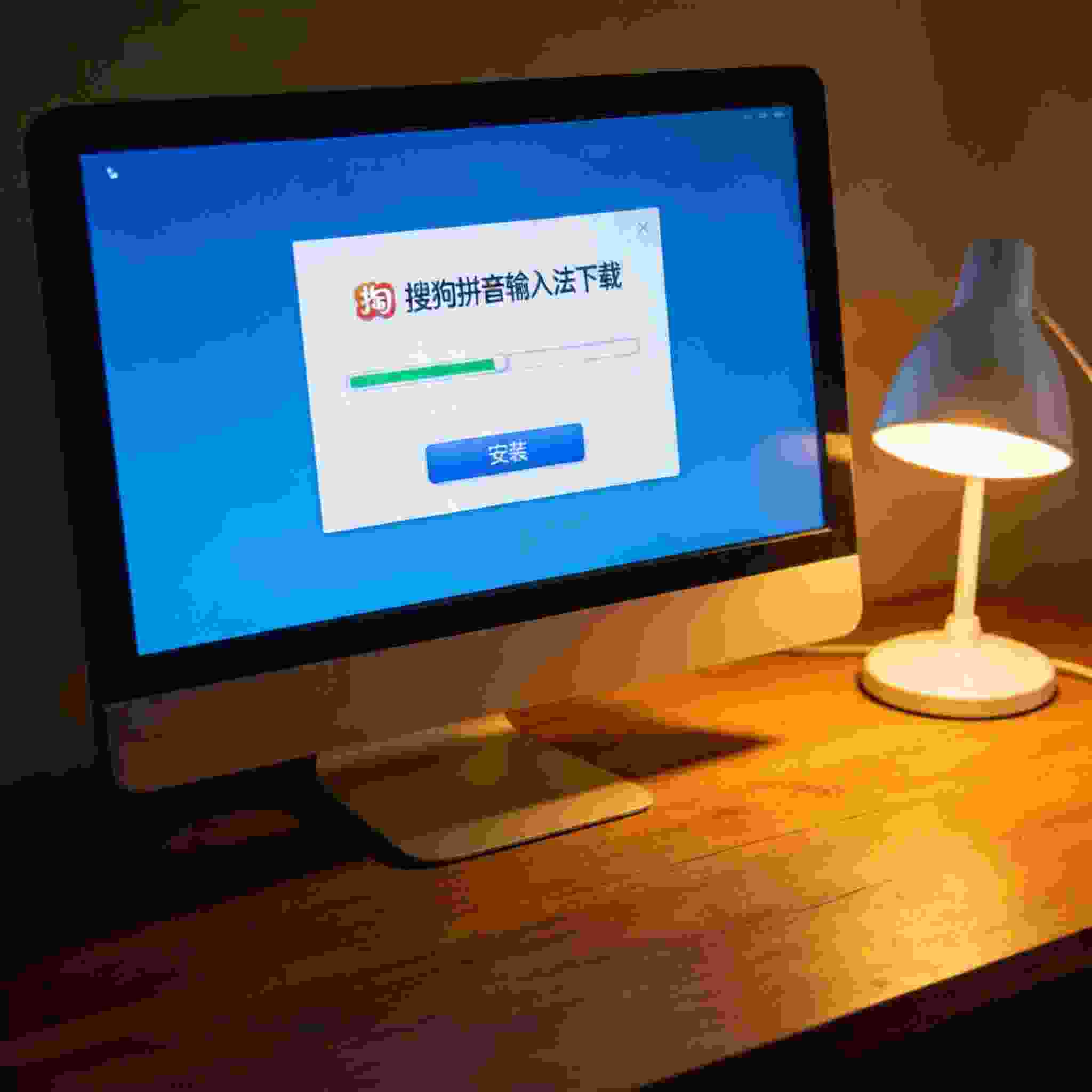 电脑桌上的电脑，屏幕显示搜狗拼音下载界面，旁边放着台灯