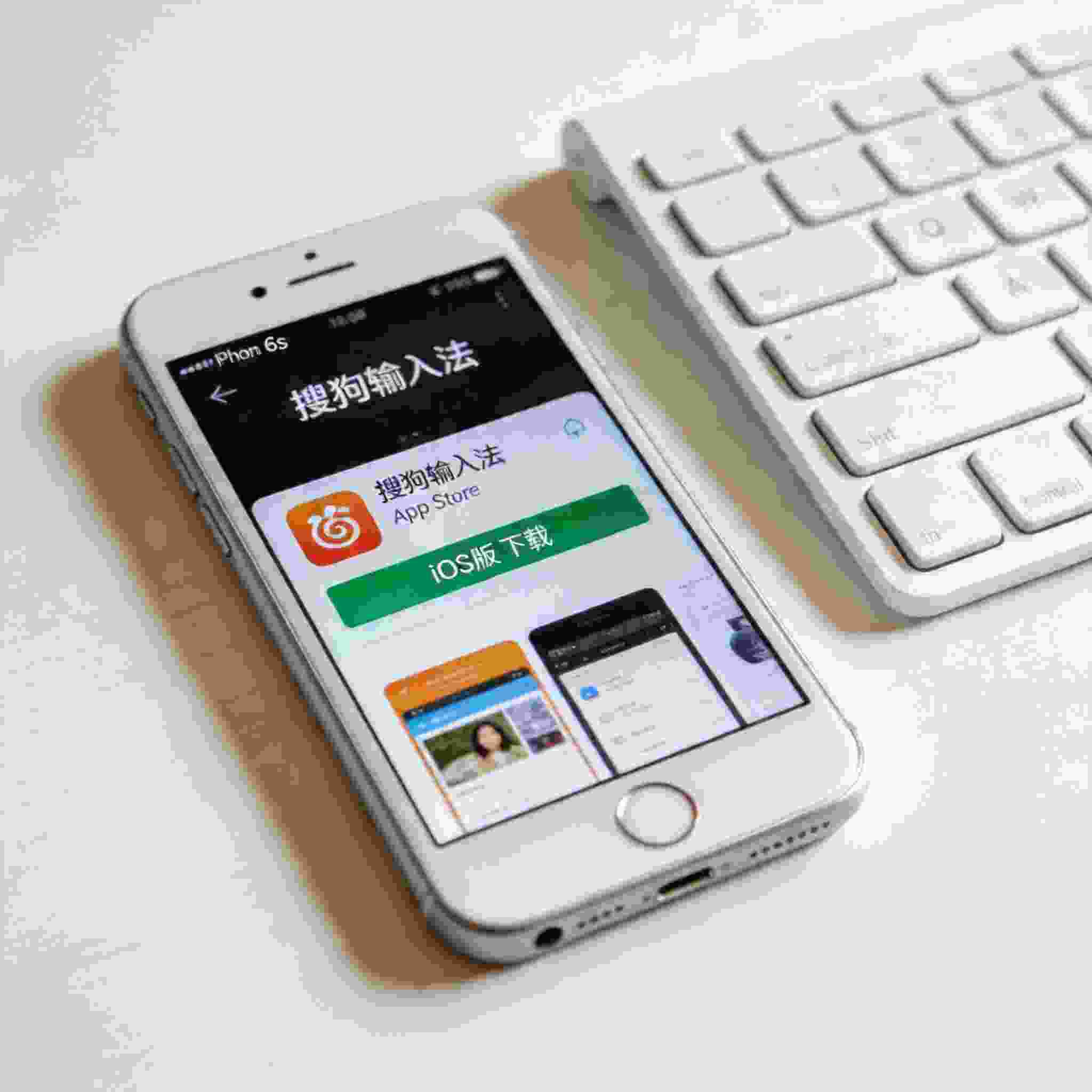 桌面放着iPhone 6s，屏幕显示App Store里的搜狗拼音输入法iOS版下载界面，旁边摆着外接键盘，室内自然光