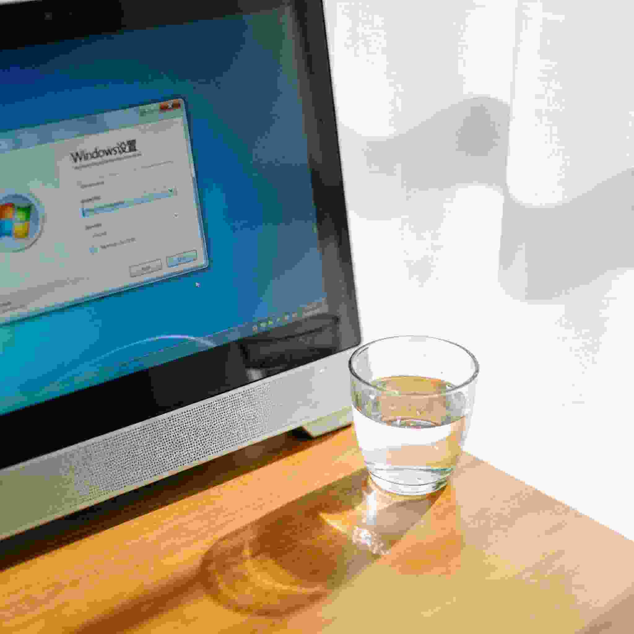书桌上的主机，屏幕显示Windows设置界面，桌角放着水杯，自然光