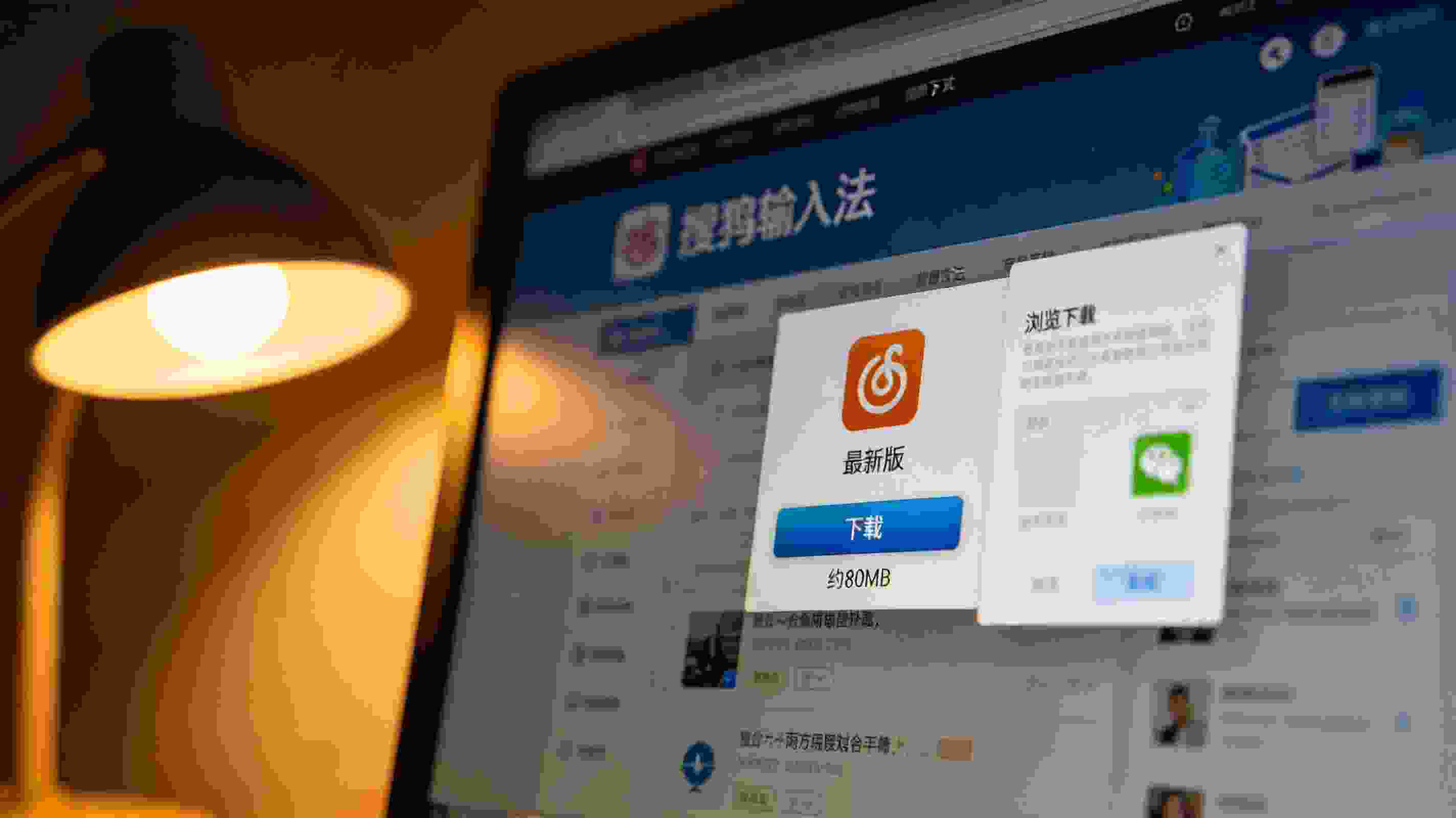 电脑屏幕显示搜狗拼音输入法官方下载页面，中间偏上的下载按钮标注最新版、约80MB，旁边弹出浏览器下载确认窗口，台灯暖光
