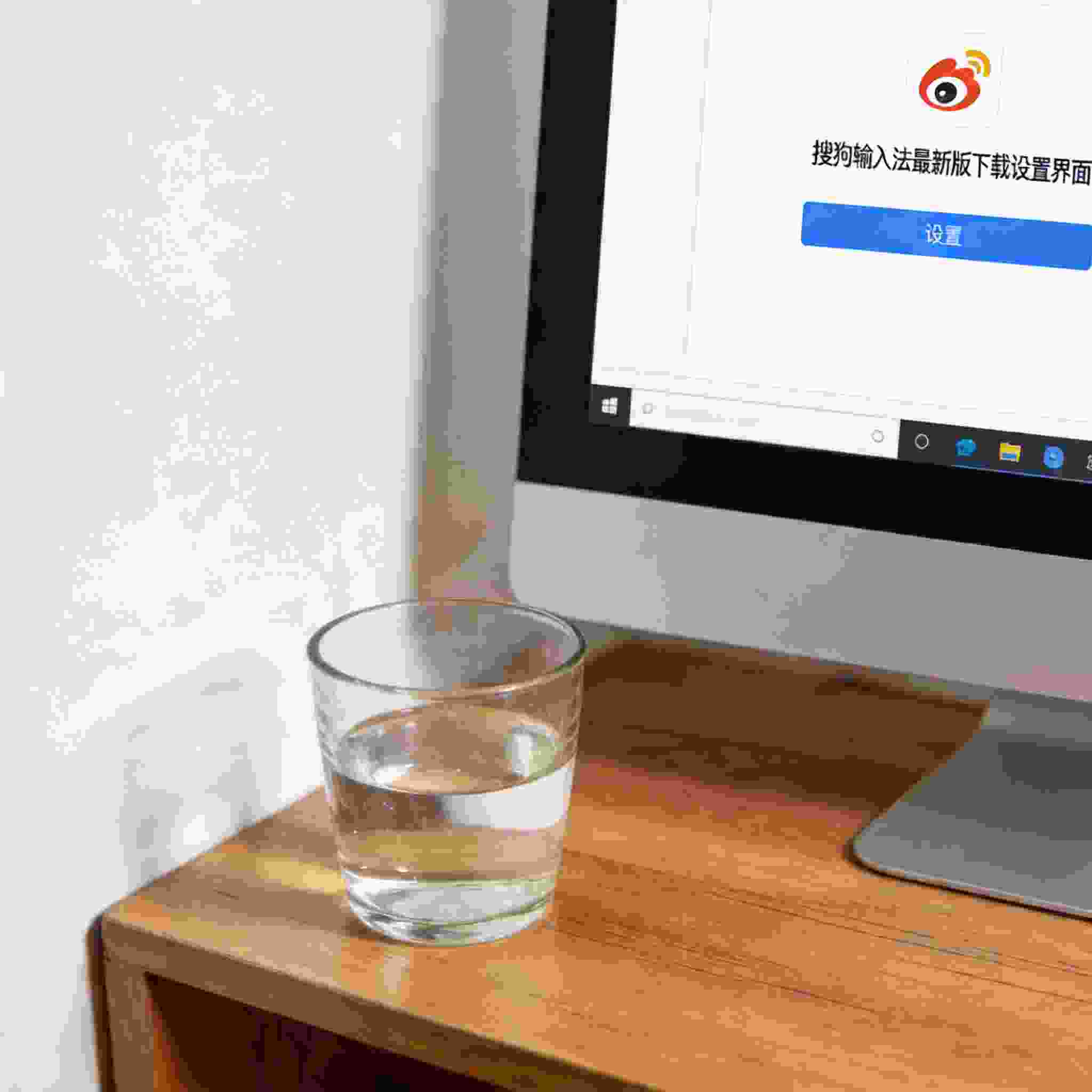 书桌上的主机，屏幕显示搜狗拼音输入法最新版下载设置界面，桌角放着水杯，自然光